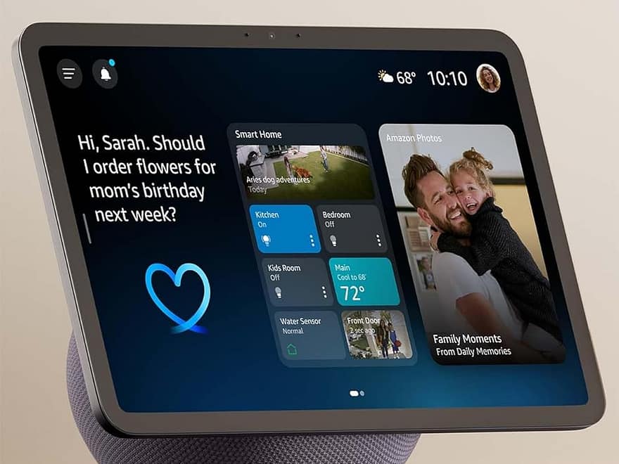 Echo Show 11 smart display on fabric speaker base with touchscreen, camera, and Alexa feature icons on a tabletop
