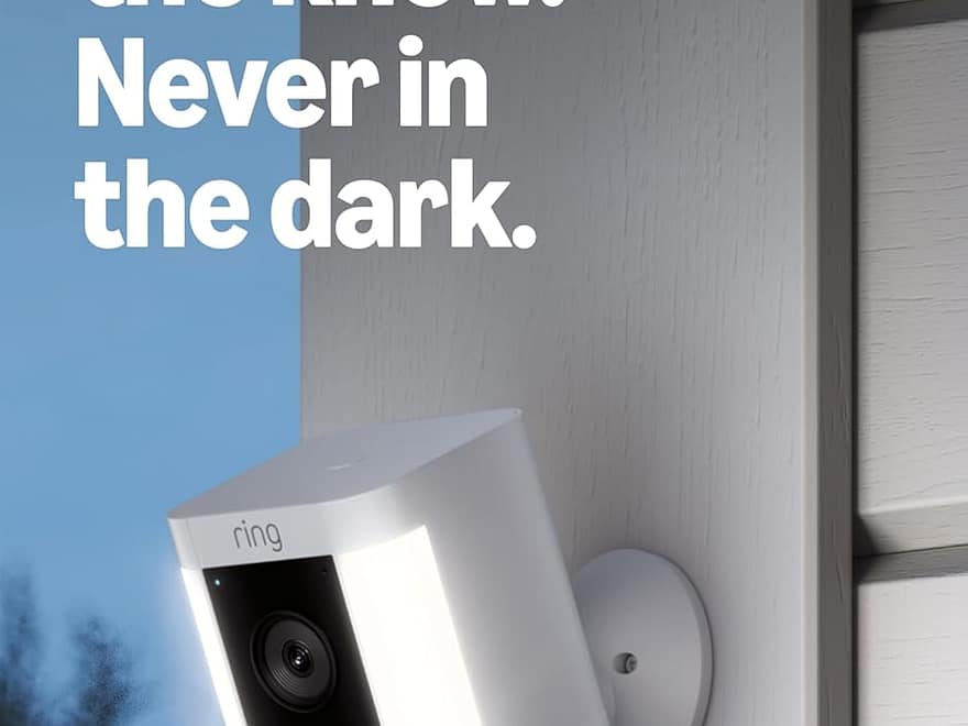 Ring Spotlight Cam Plus Battery white wall-mounted security camera with dual lights on exterior siding