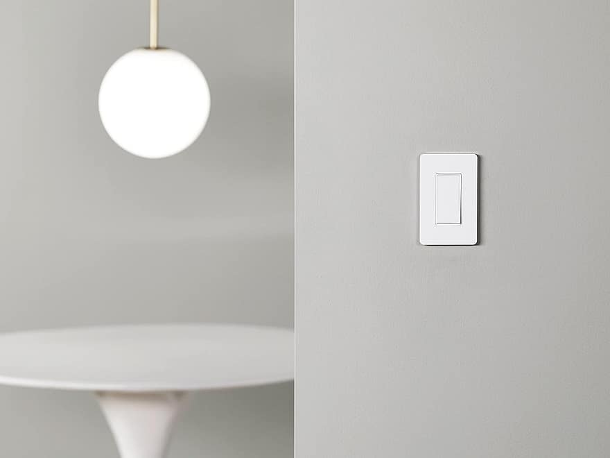 Amazon Basics smart light switch single pole in white finish on a gray wall beside a glowing pendant light.